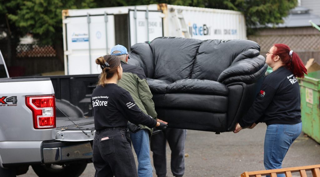 ReStore volunteers carrying a donated sofa from truck into the store