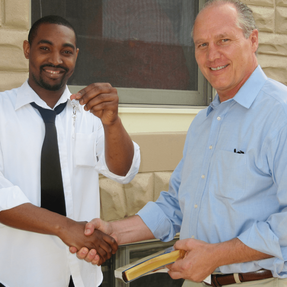 Mike Posko shaking hand smiling with new homeowner as he holds up his new key to his home